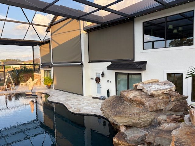 A pool lanai with a motorized screen lowered beside a rock waterfall