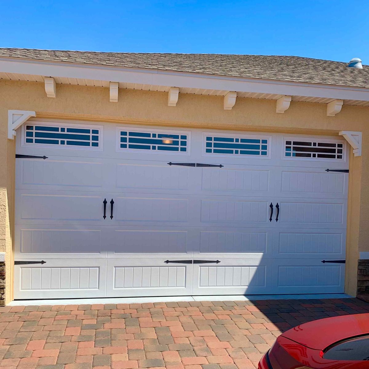 A white carriage-style garage door repaired and closed above a paver driveway