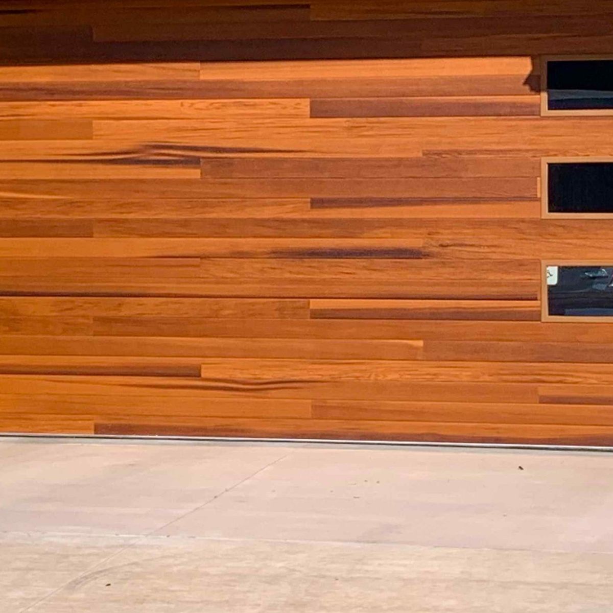 A wood-look replacement garage door with dark window panels on a stucco home